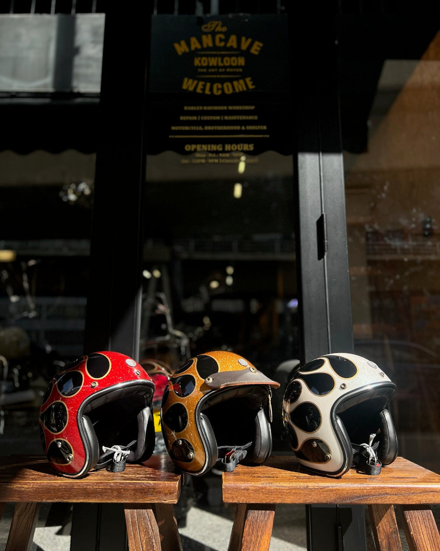 Three motorcycle helmets with unique designs on a wooden surface, with a background sign reading 'Man Cave'.