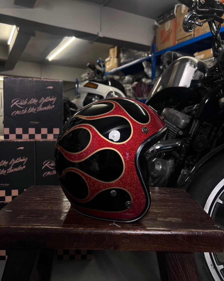 Flamed red and black motorcycle helmet on a wooden surface with a motorcycle in the background.