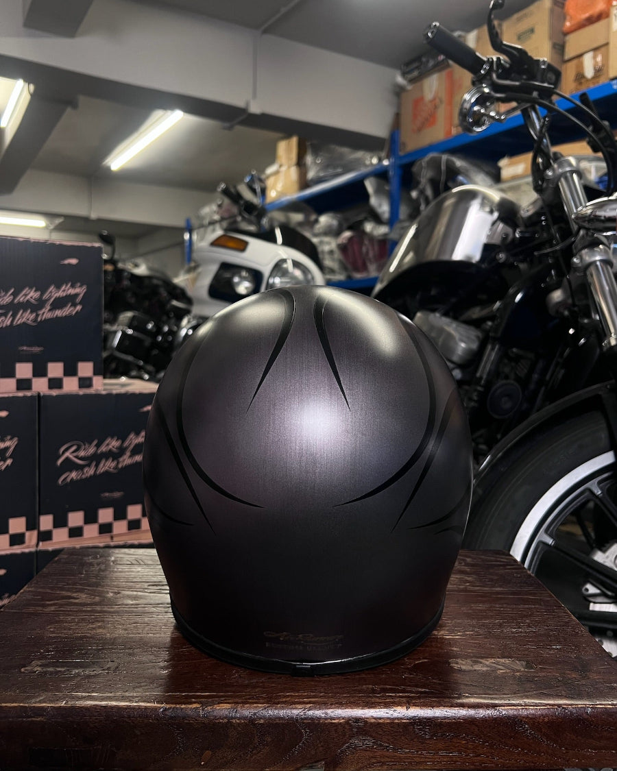 Black motorcycle helmet on a wooden surface with a motorcycle and boxes in the background
