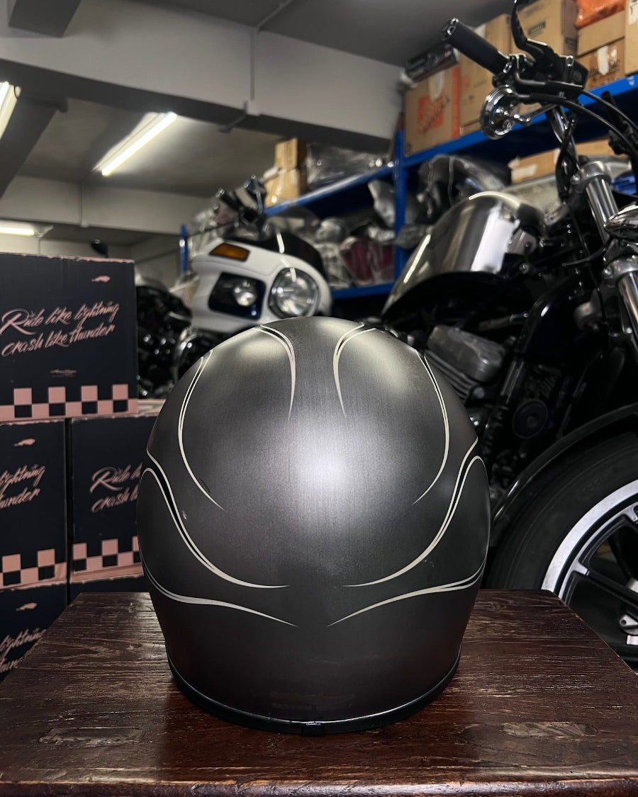 Black motorcycle helmet with white designs on a wooden surface in a warehouse setting.