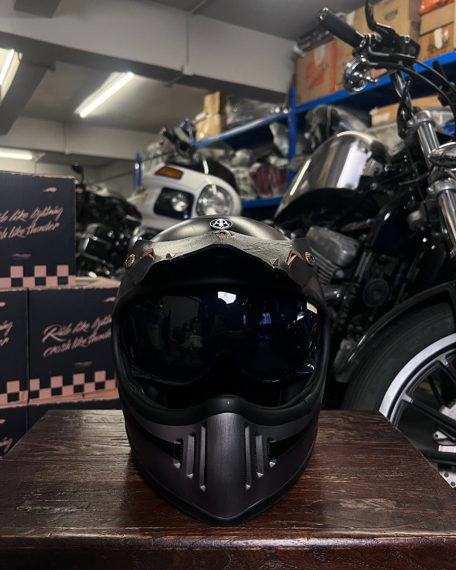 Black motorcycle helmet on a wooden surface with a motorcycle and boxes in the background