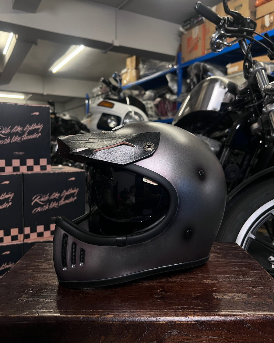 Black motorcycle helmet on a wooden surface with a motorcycle and boxes in the background