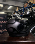 Black motorcycle helmet on a wooden surface with a motorcycle in the background.