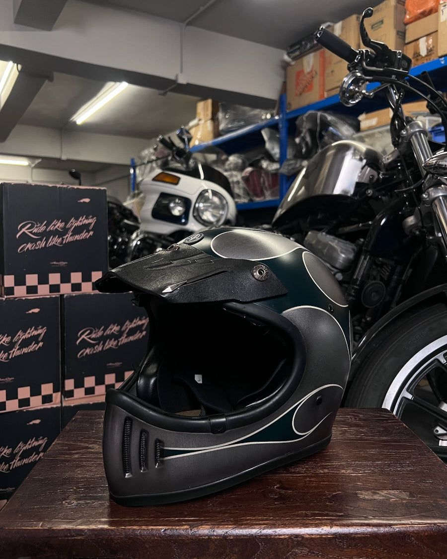 Black motorcycle helmet on a wooden surface with a motorcycle and boxes in the background