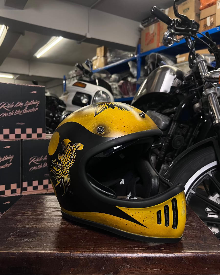 Yellow and black helmet on a wooden surface with motorcycles and boxes in the background