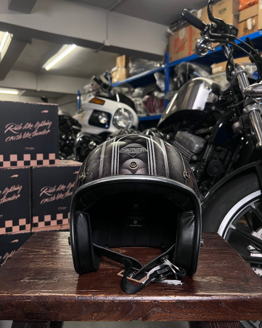 Black leather motorcycle helmet on a wooden surface with motorcycles and boxes in the background.