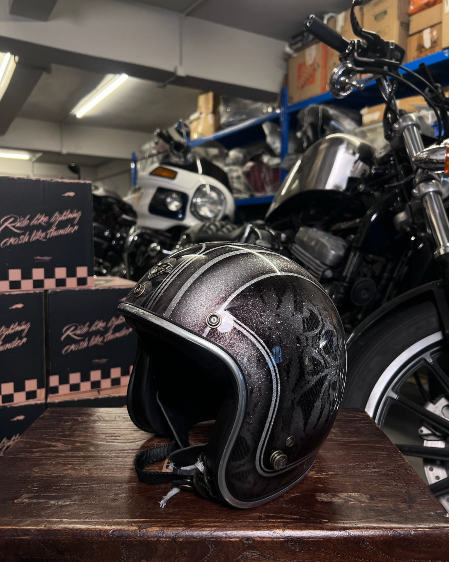 Black motorcycle helmet with decorative patterns on a wooden surface, with a motorcycle and boxes in the background.