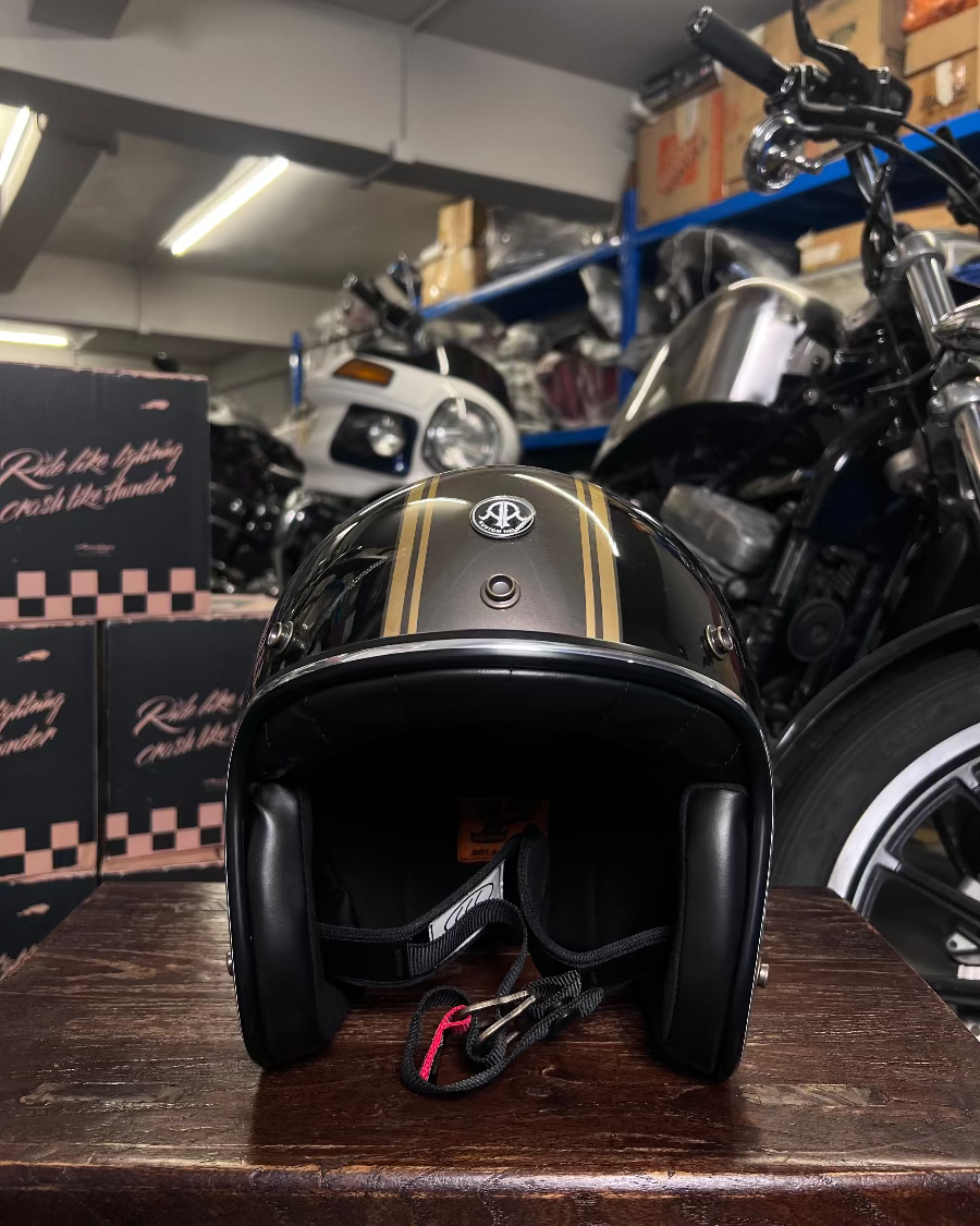 Black motorcycle helmet with gold accents on a wooden surface in a garage setting.