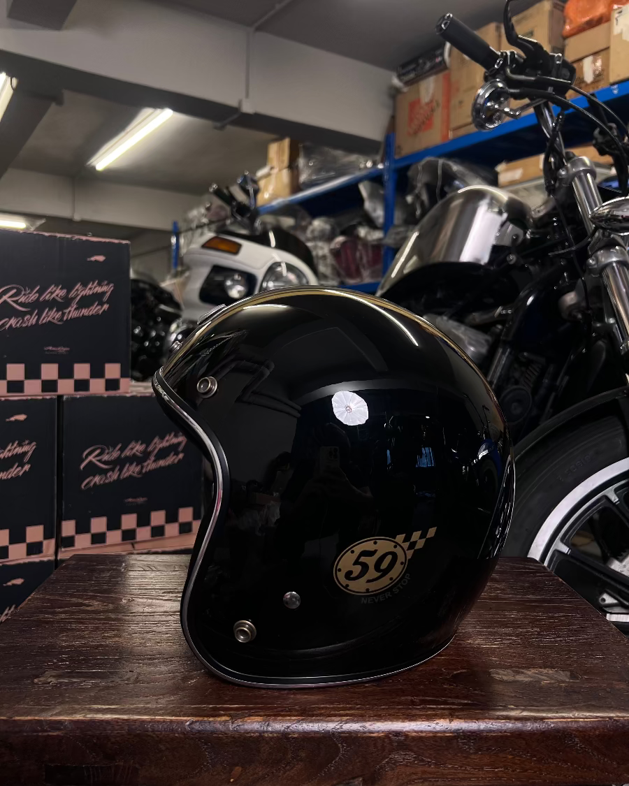 Black motorcycle helmet with number 50 on a wooden surface, with a motorcycle and boxes in the background.