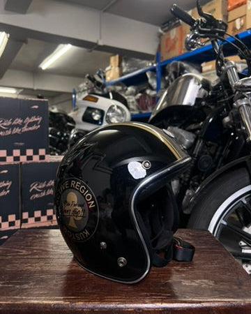 Black helmet with 'Blue Region' logo on a wooden surface in a garage setting with motorcycles.