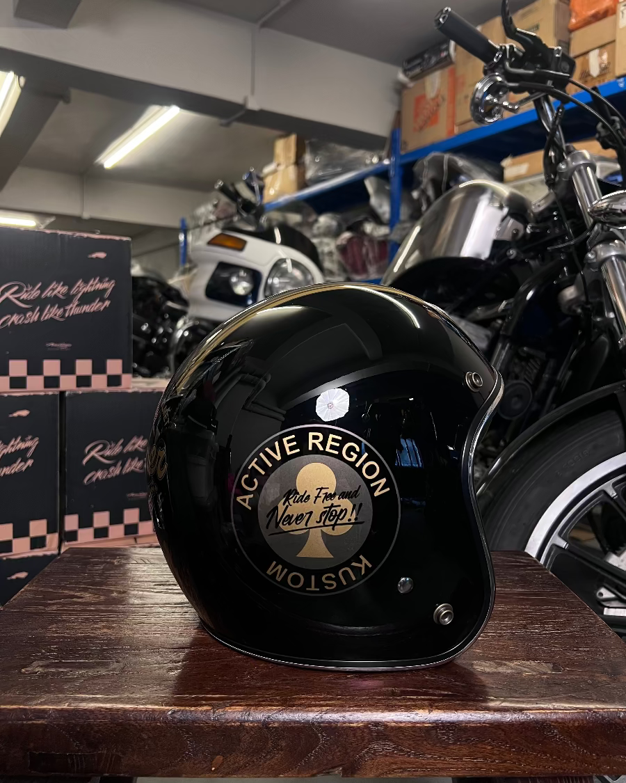 Black helmet with 'Active Region Kustom' logo on a wooden surface with motorcycles in the background.