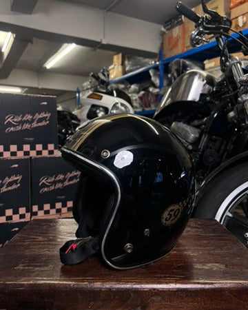 Black motorcycle helmet on a wooden surface with a motorcycle in the background