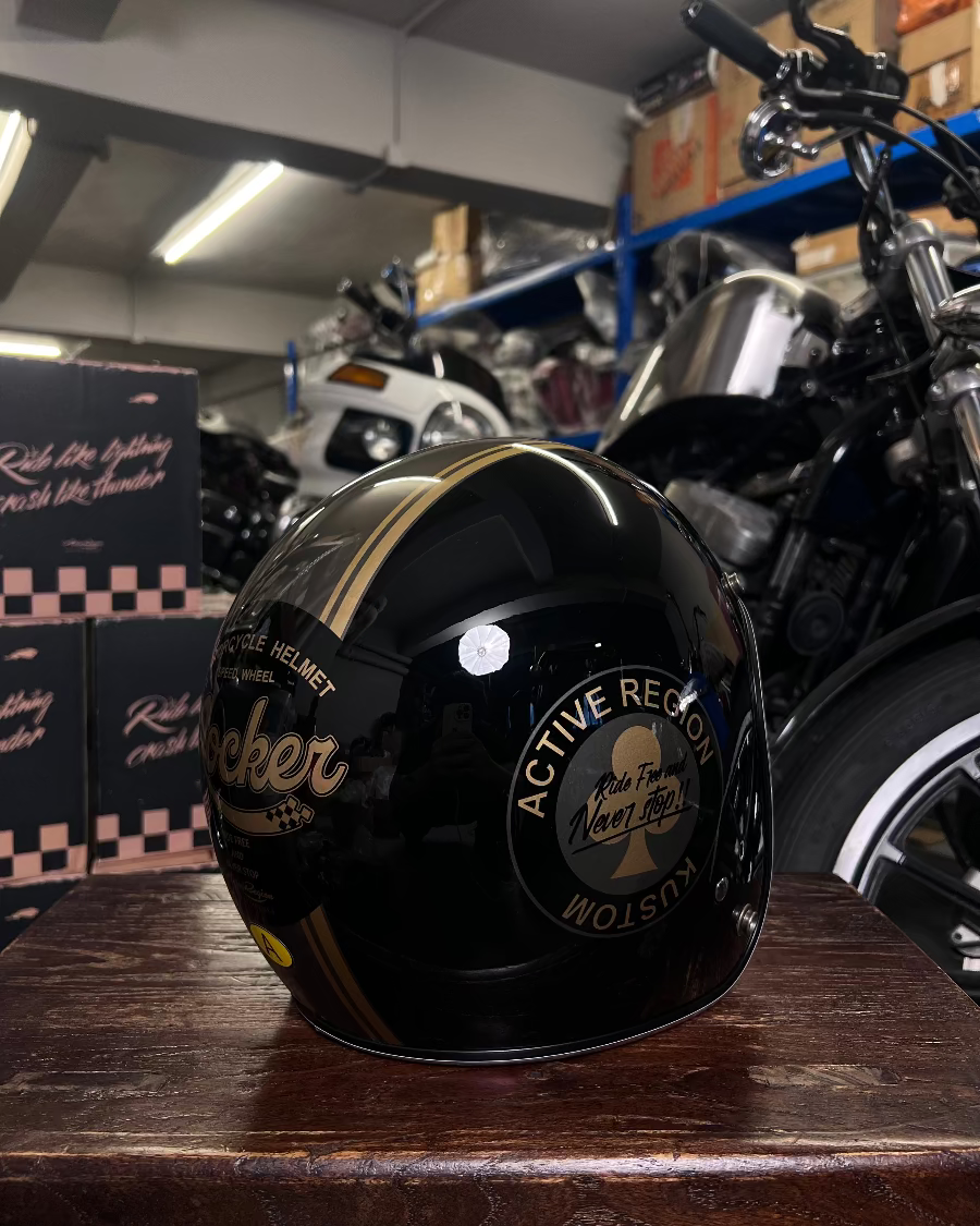Black motorcycle helmet with gold accents on a wooden surface in a garage setting.