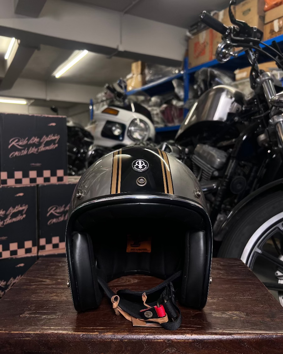 Black motorcycle helmet with gold stripes on a wooden surface in a garage setting.