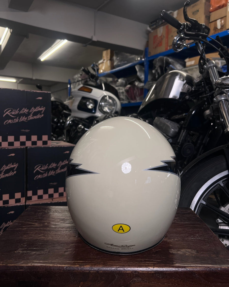 White motorcycle helmet with blue designs on a wooden surface, with motorcycles and boxes in the background.