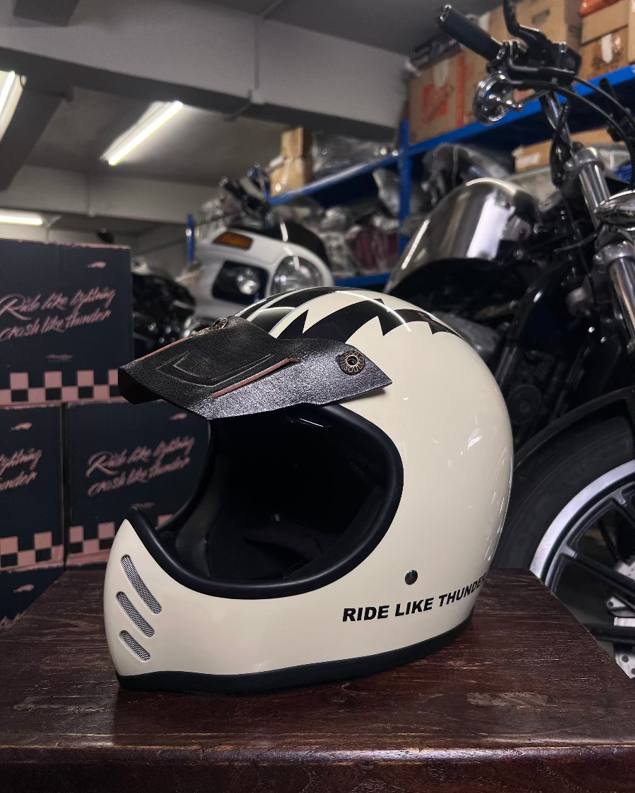 White motorcycle helmet with 'Ride Like Thunder' text on a wooden surface in a garage setting.