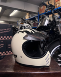 White motorcycle helmet on a wooden surface with motorcycles and boxes in the background