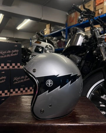 Silver motorcycle helmet with black design on a wooden surface in a garage setting.