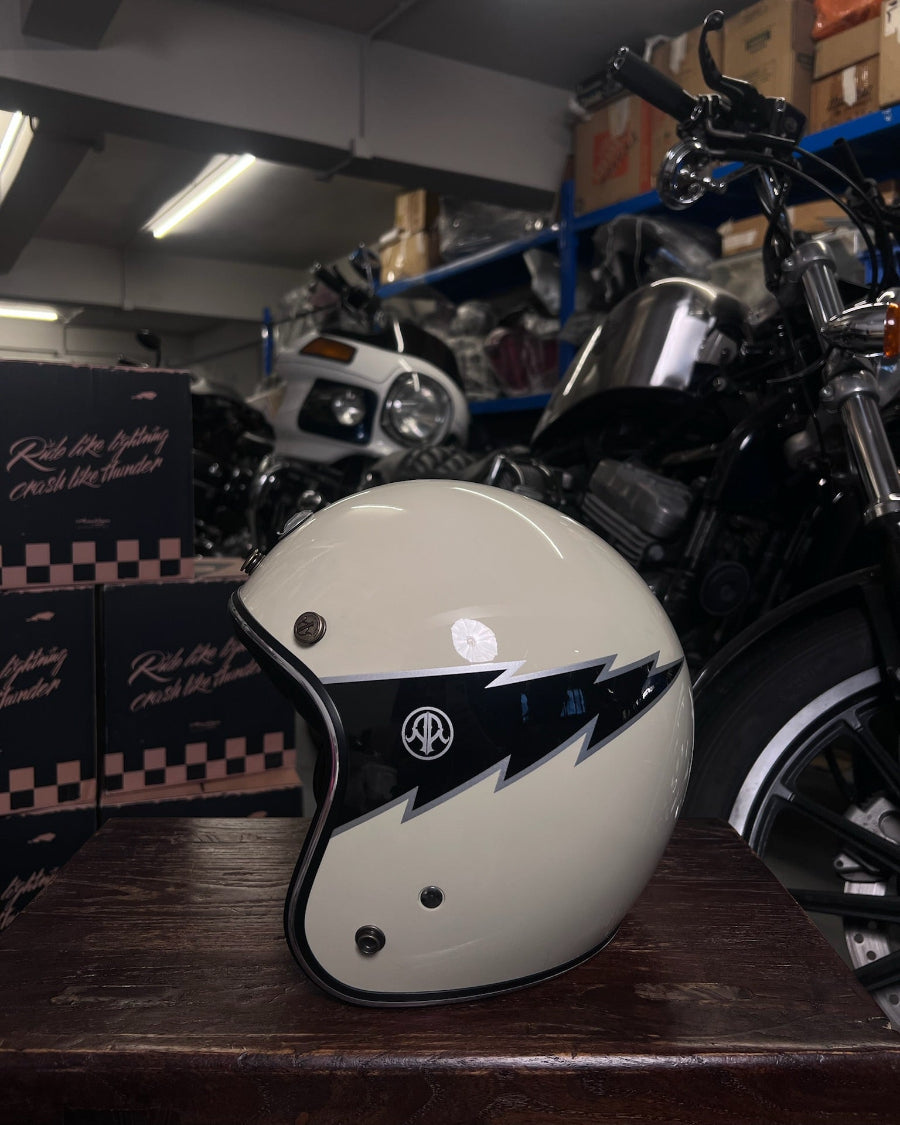 White motorcycle helmet with black design on a wooden surface, with a motorcycle and boxes in the background.